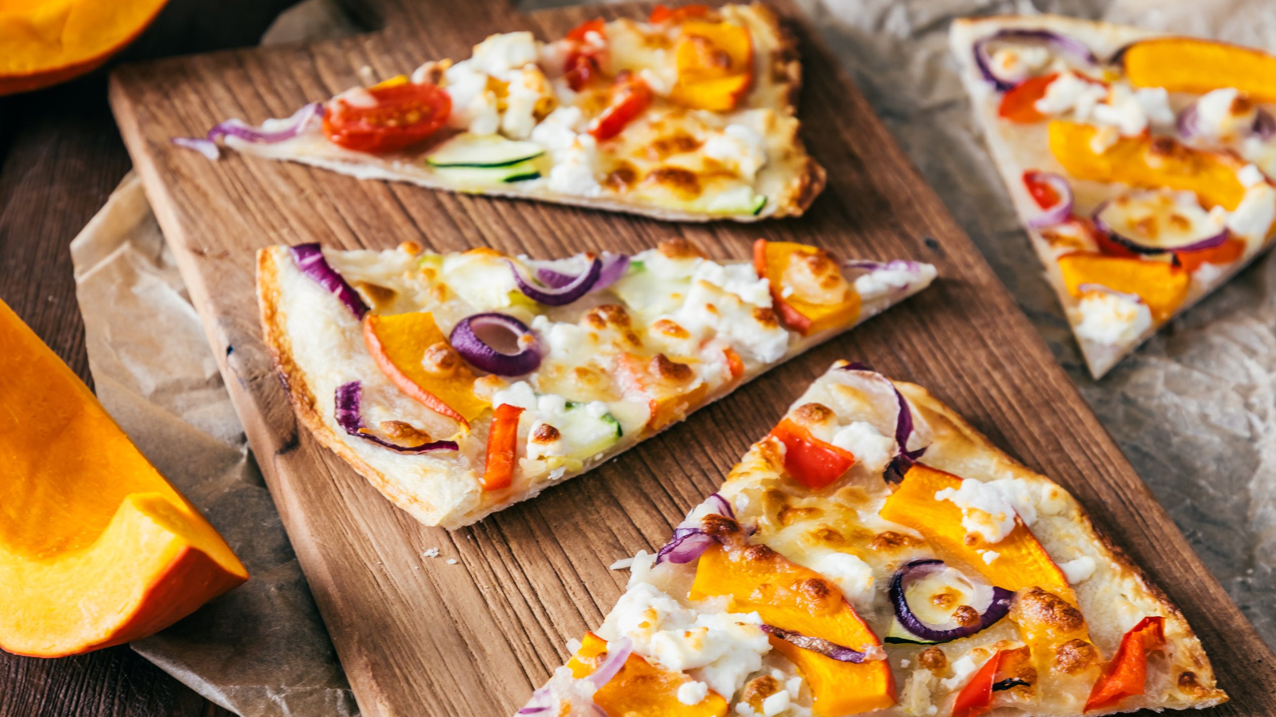 Pieces of tarte flambee with pumpkin, red onions and cheese on a wooden board