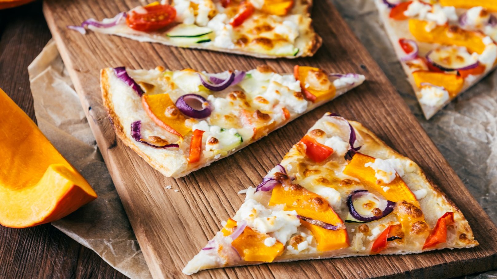 Pieces of tarte flambee with pumpkin, red onions and cheese on a wooden board